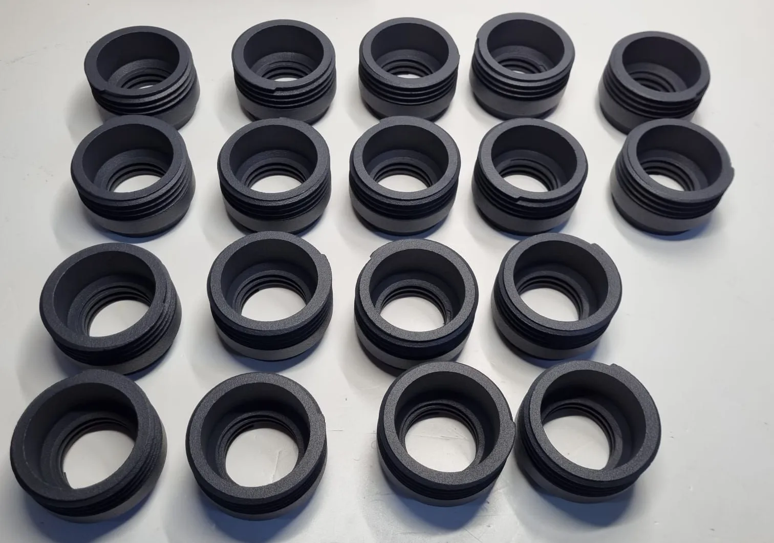 Eighteen black PA12 nylon attachments in rows on a white bench, their outer threads and inner threads both visible