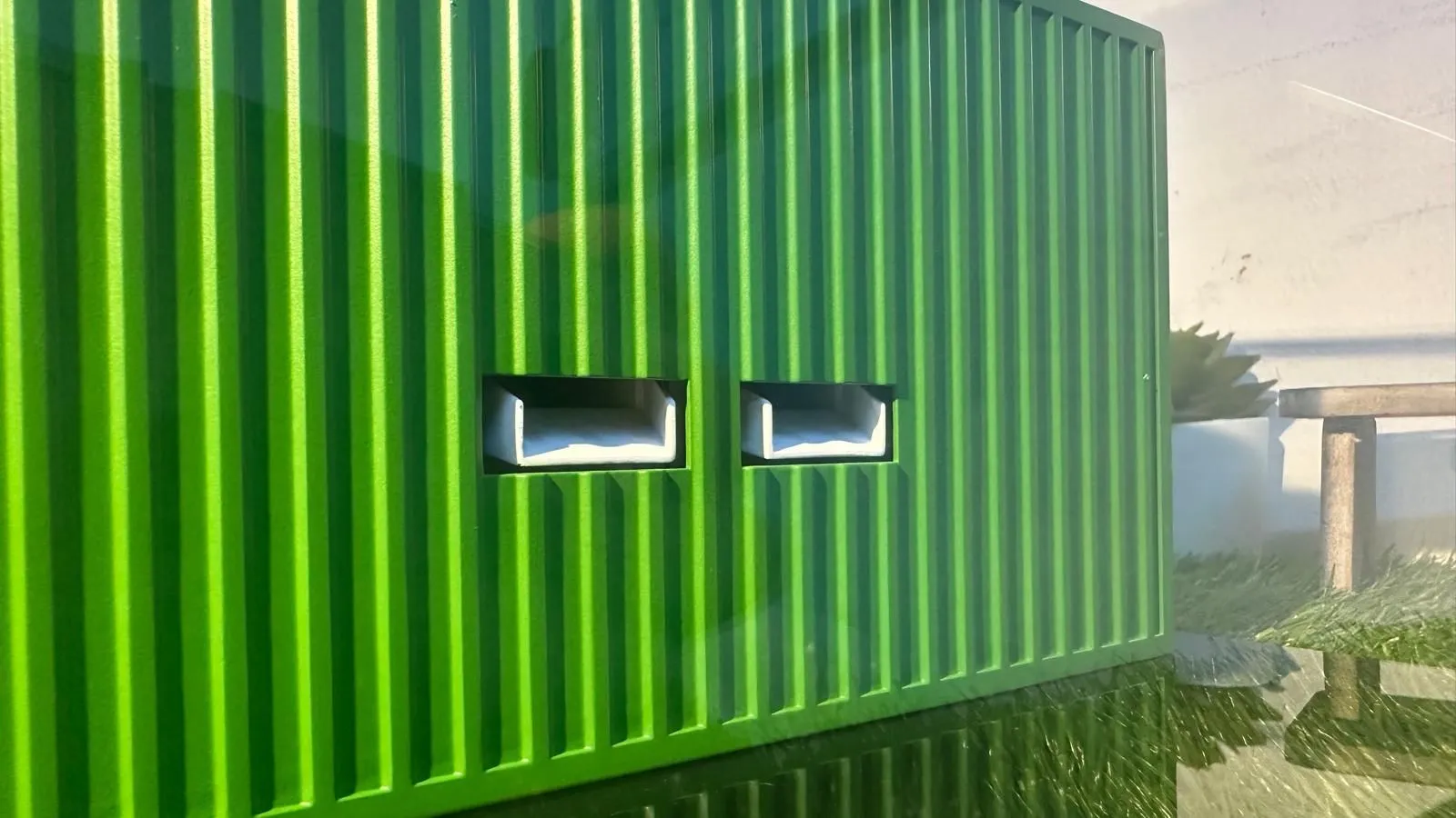 Close-up of the green ribbed container wall with two rectangular openings, the white chute trays of the machine showing through them