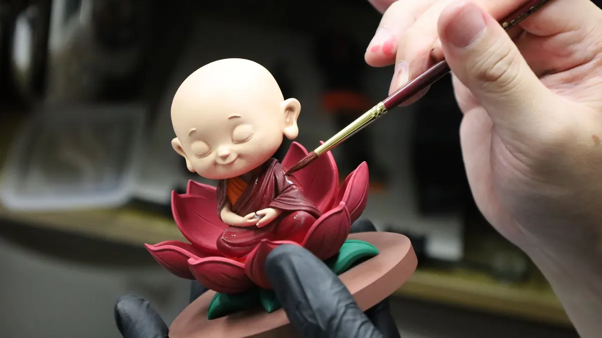 Additive Inn artist hand-painting the face of a Mini Me monk figurine