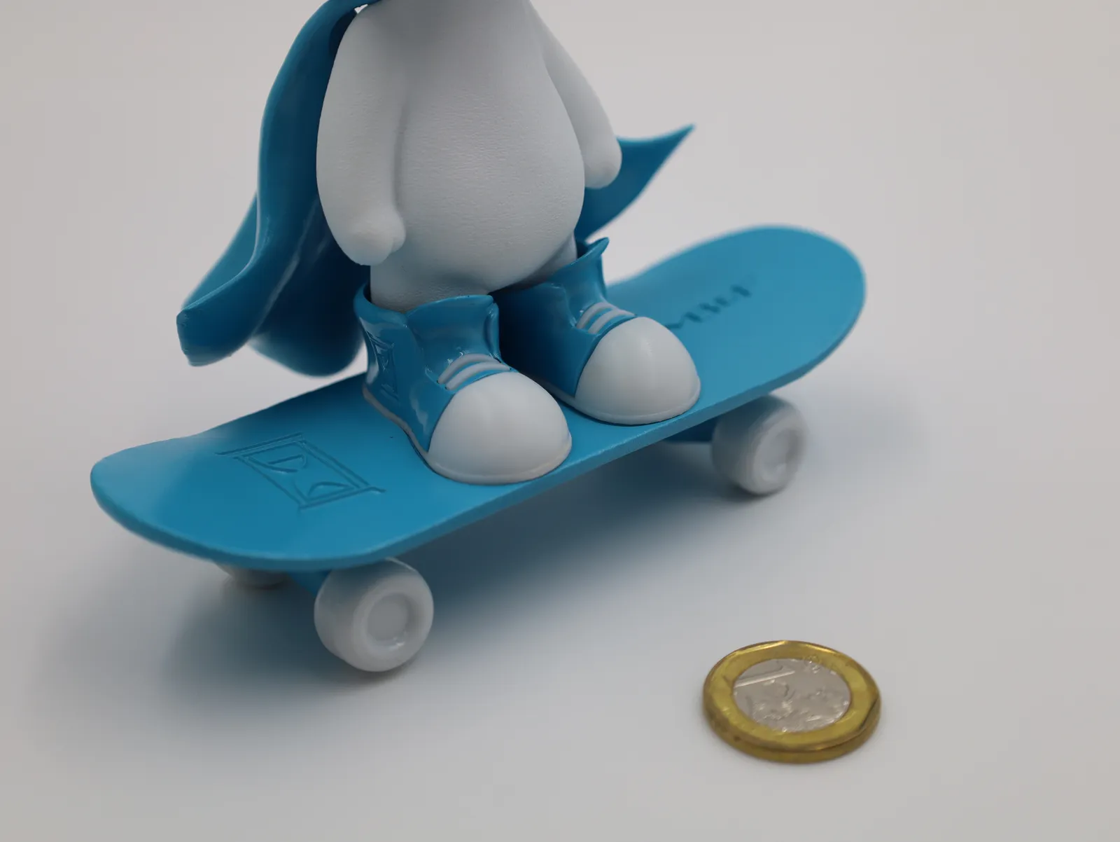 A white Minimilian figure in a blue cape and blue shoes standing on a blue skateboard, from the first painted sample set
