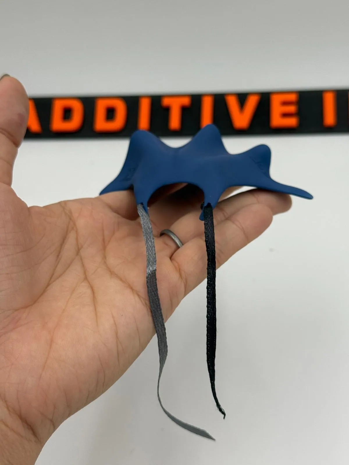 A hand holding the thinner blue cape with a dark ribbon trailing from its neck