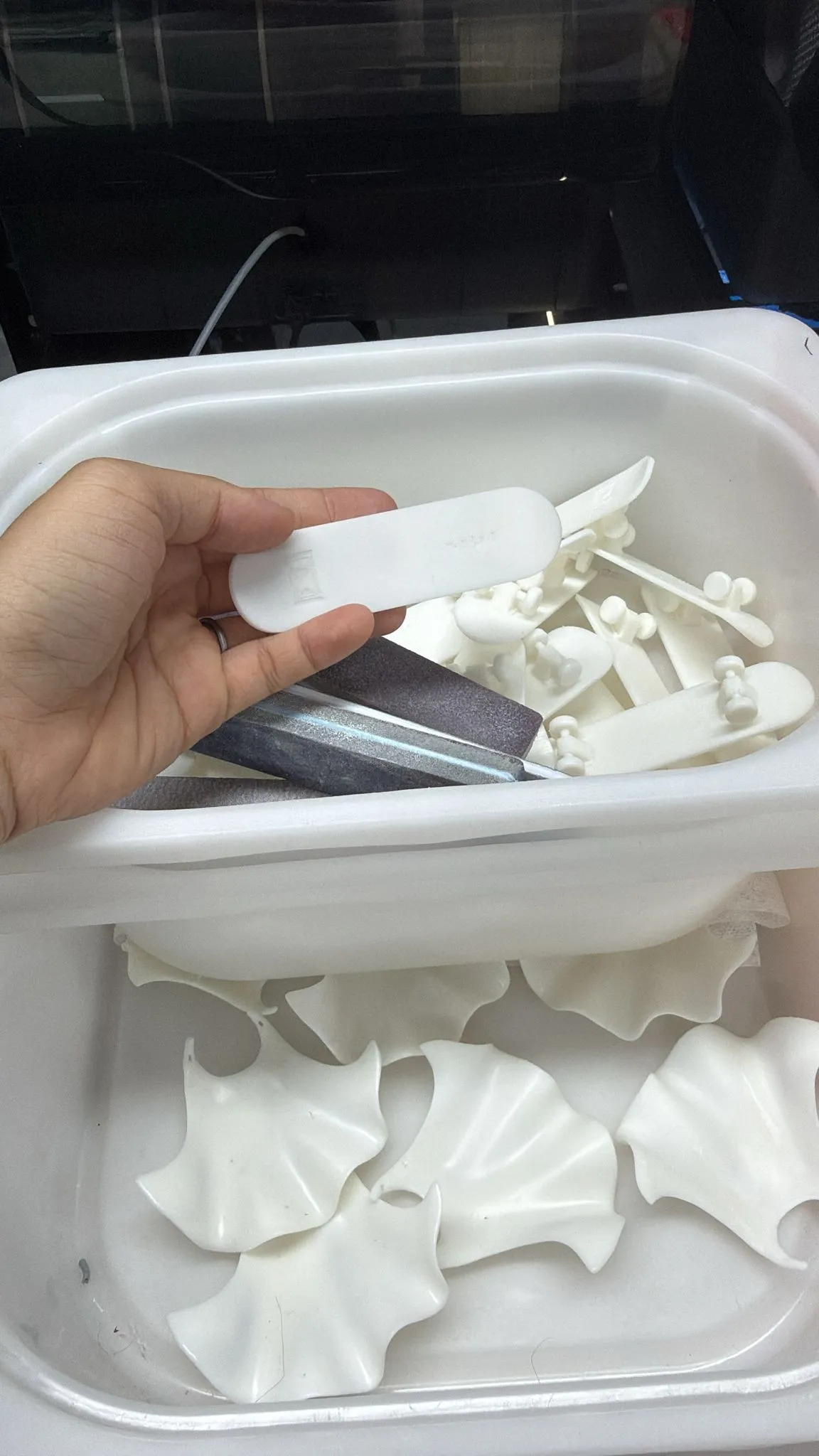 A tub of freshly printed white capes and skateboards, with a hand holding one skateboard