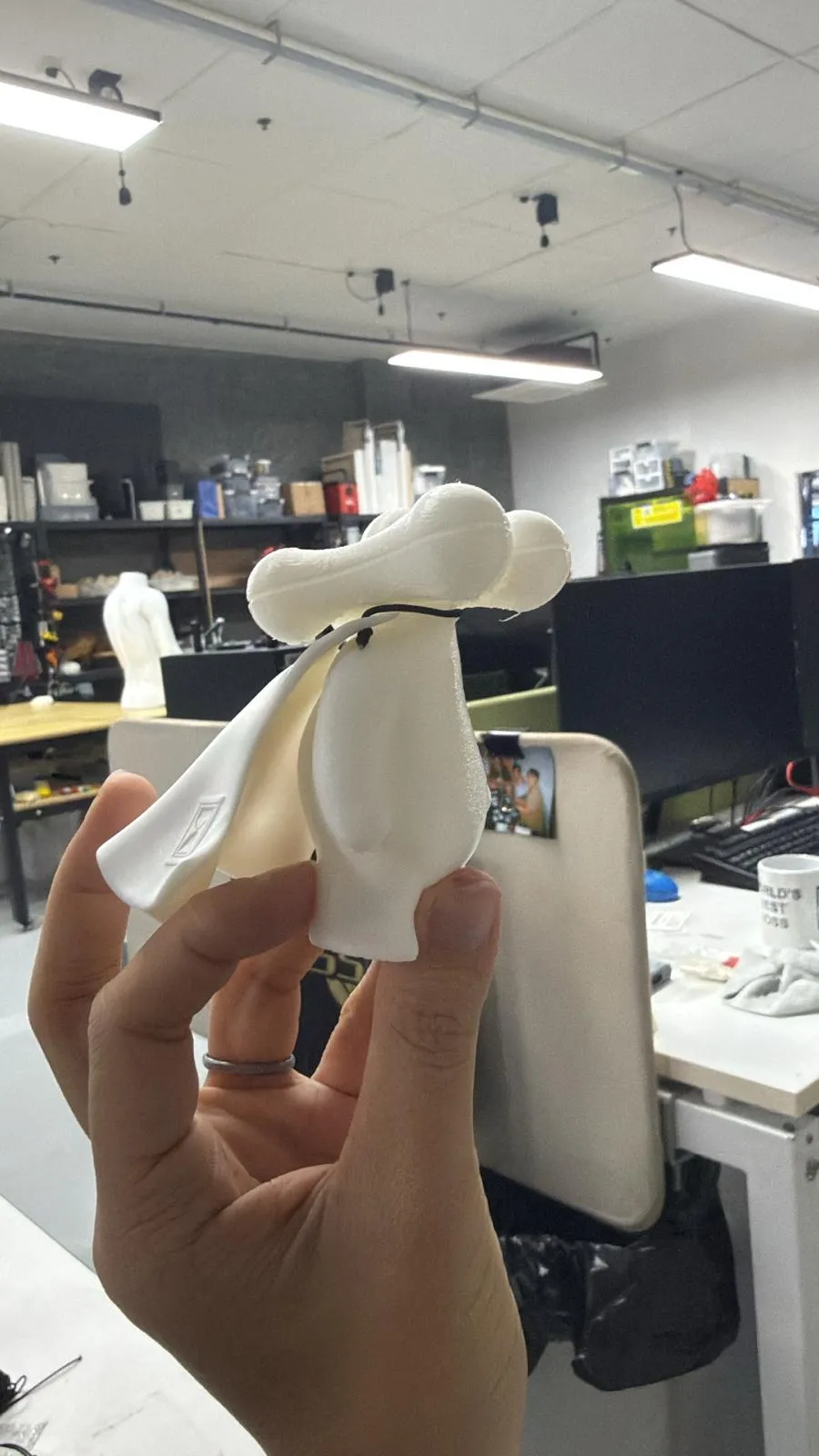 A hand holding a white figure wearing a cape tied at the neck with a short black rubber band