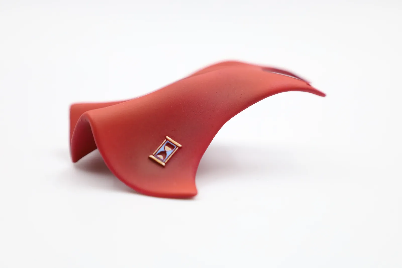 A finished red cape on a white background, the hour glass icon debossed on its swept side