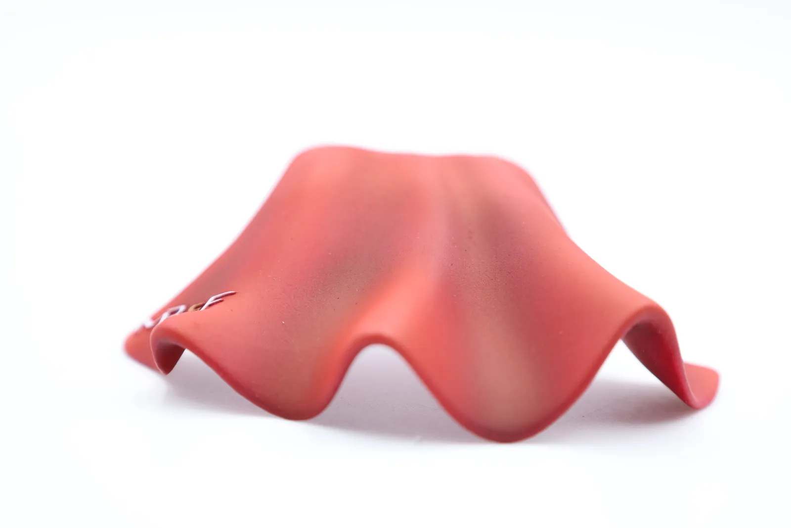 A finished red cape seen from behind, its wavy hem spread out on a white background