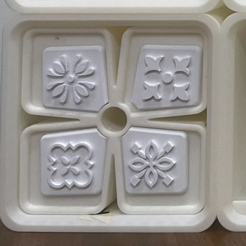 Close-up of one tiled front: four square relief tiles with different floral and lattice patterns, set on the petals around a central finger hole
