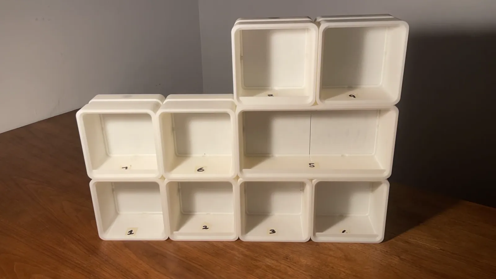 Nine bare printed boxes stacked on a wooden table before any fronts go on: four along the bottom, two singles and the long double-width box above, two more on top, each with a handwritten number
