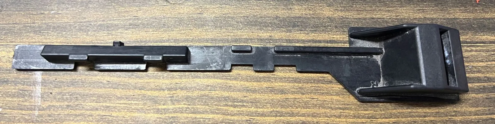 The client's original black latch arm on a wooden table, scuffed and worn, with its square catch at the right-hand end