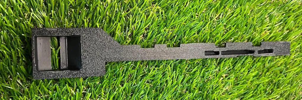 The underside of the printed latch arm on grass, with the textured finish from the print bed and the open square catch