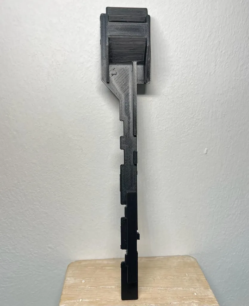 The printed latch arm standing upright against a white wall, its notched edge and rails seen side on
