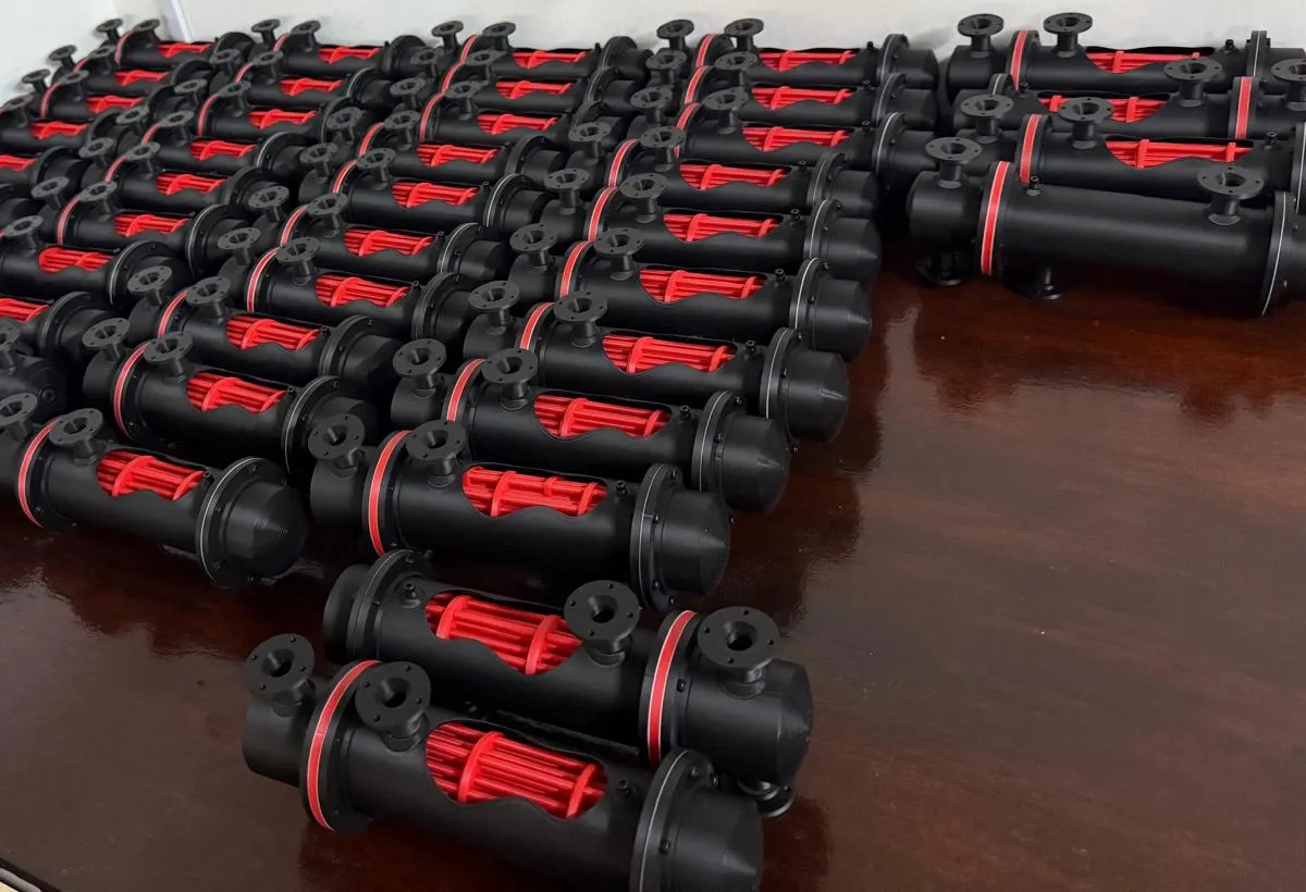 Rows of finished black heat exchanger models on a table, each shell cut open to show a red tube bundle inside