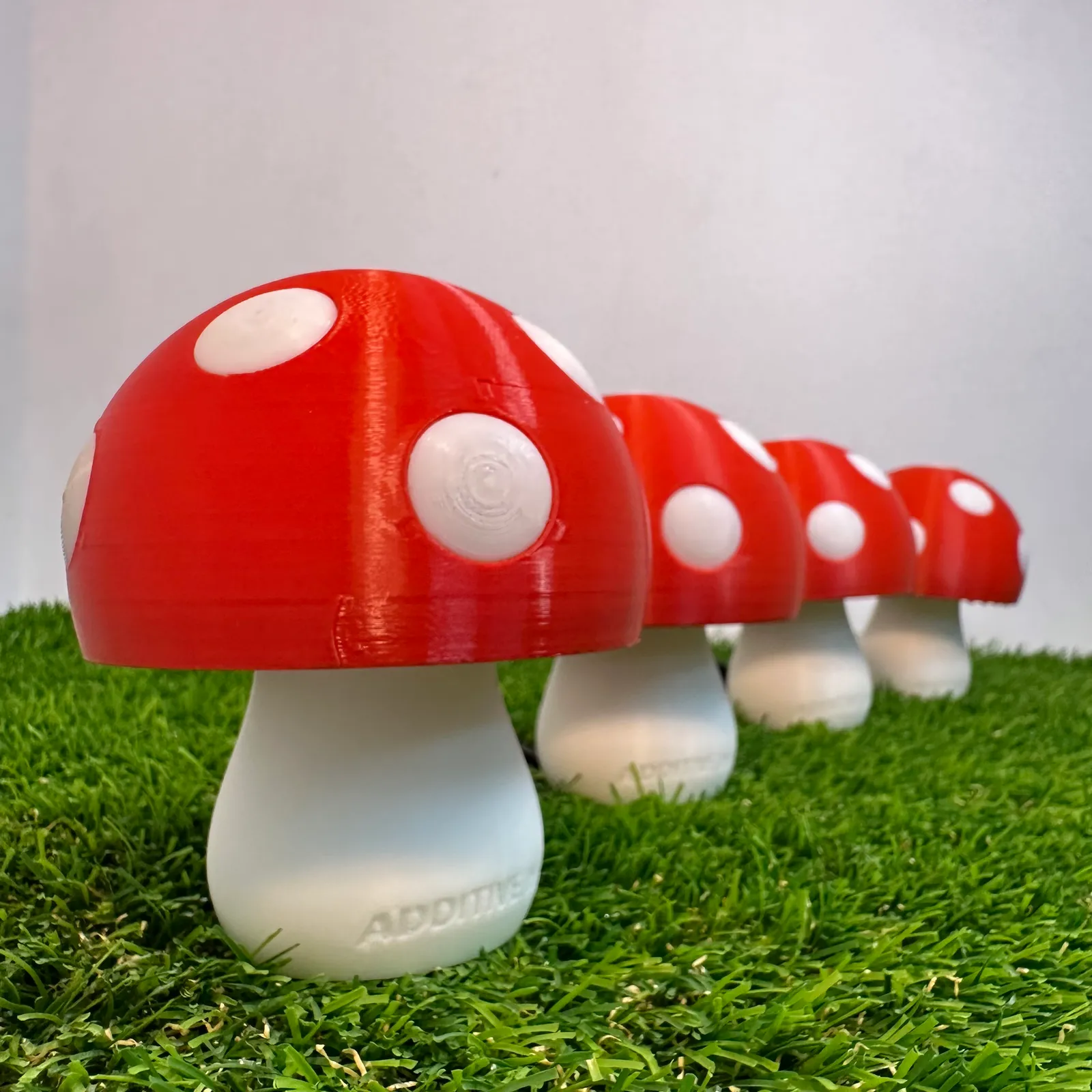 A row of five unlit mushroom lamps on artificial grass, red caps with white spots and ADDITIVE INN raised on the nearest stem