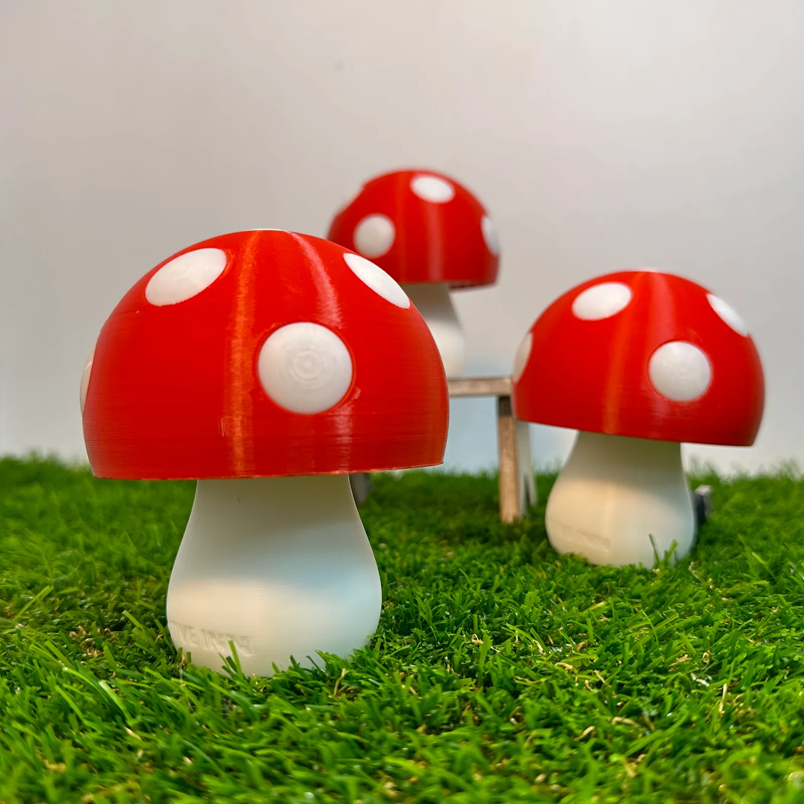 Three unlit mushroom lamps on artificial grass, one in front and two behind beside a small wooden bench