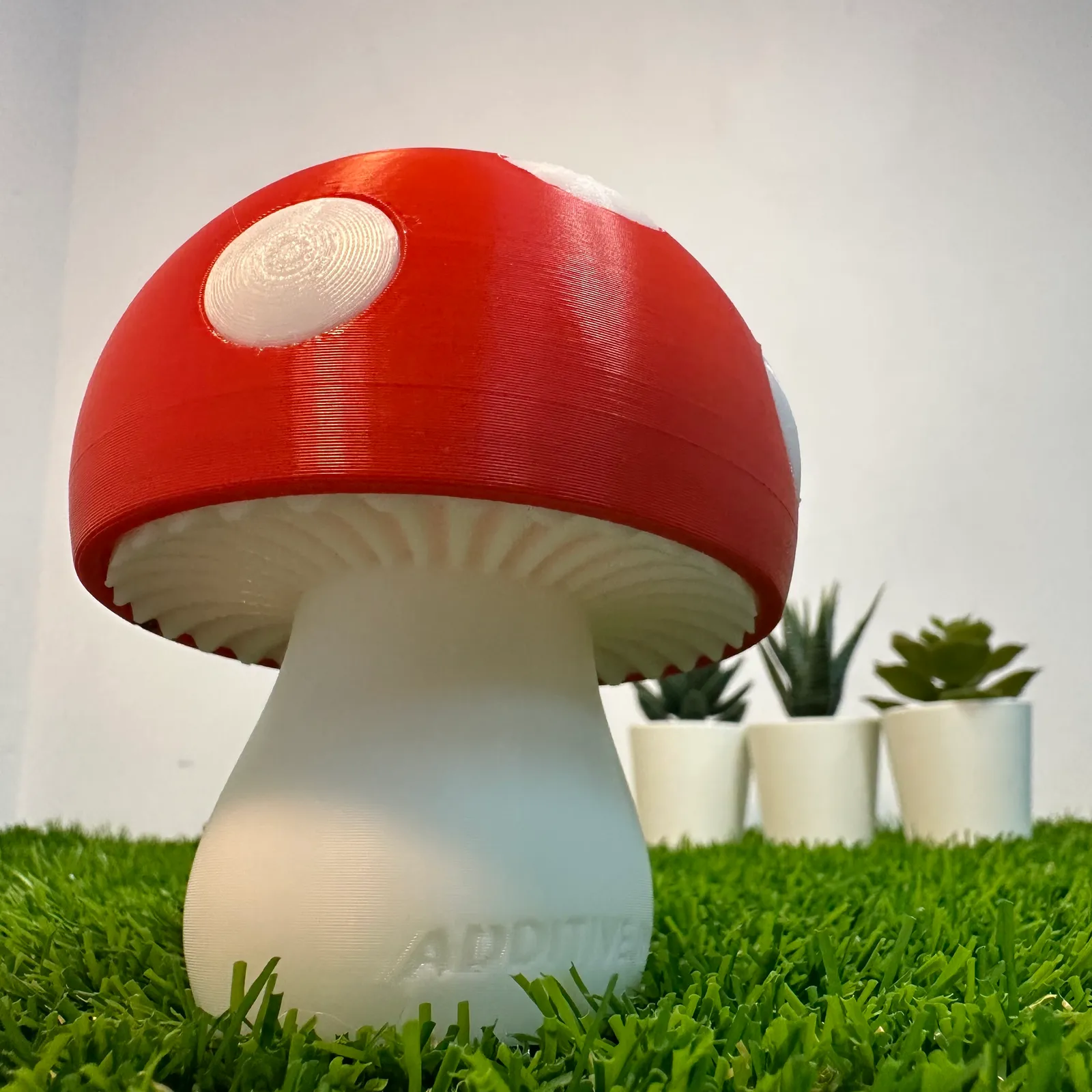 A low view of an unlit mushroom lamp showing the printed gills under the red cap and ADDITIVE INN raised on the white stem