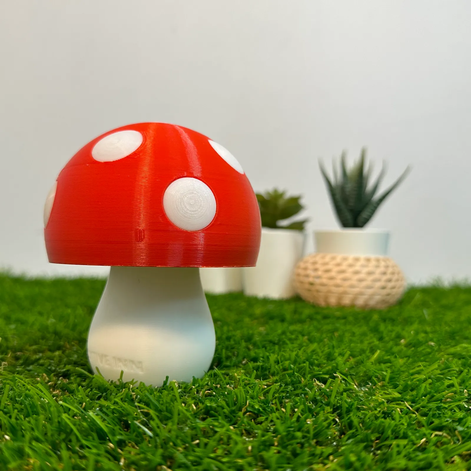 A finished mushroom lamp, unlit, on artificial grass in front of potted plants