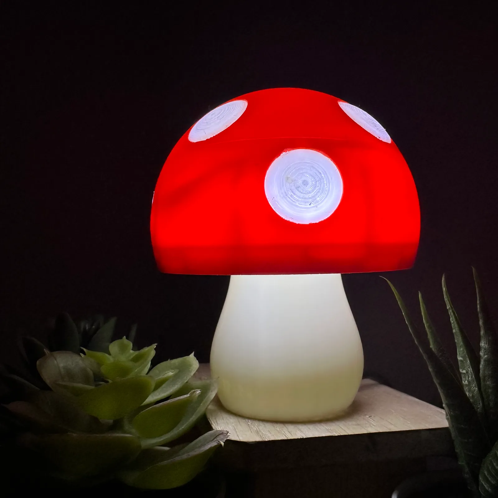 A finished mushroom lamp glowing white in a dark room, its spots brighter than the red cap