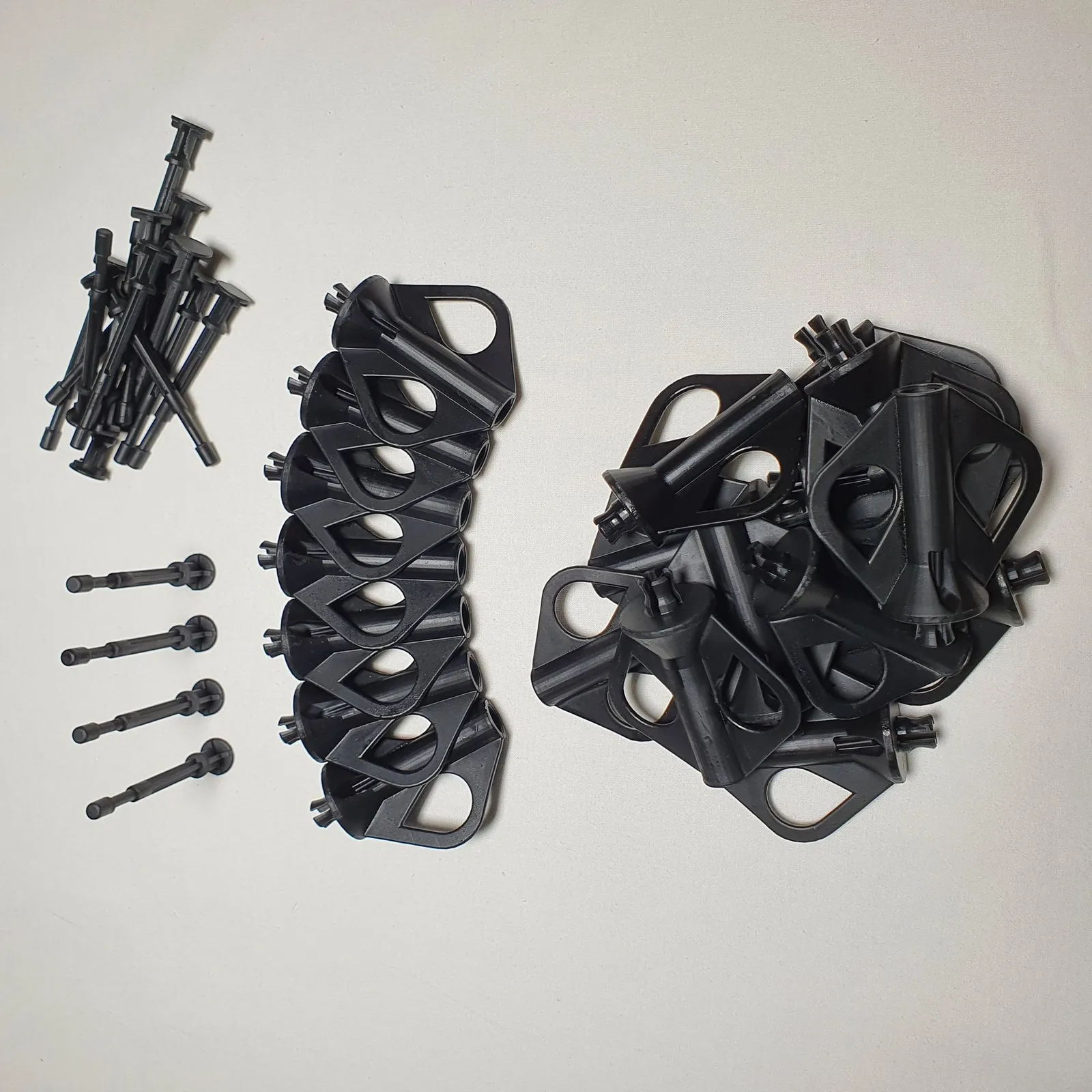 The finished batch of black resin nozzle extractors on a white table: plungers on the left, tool bodies stacked in a row and more in a pile