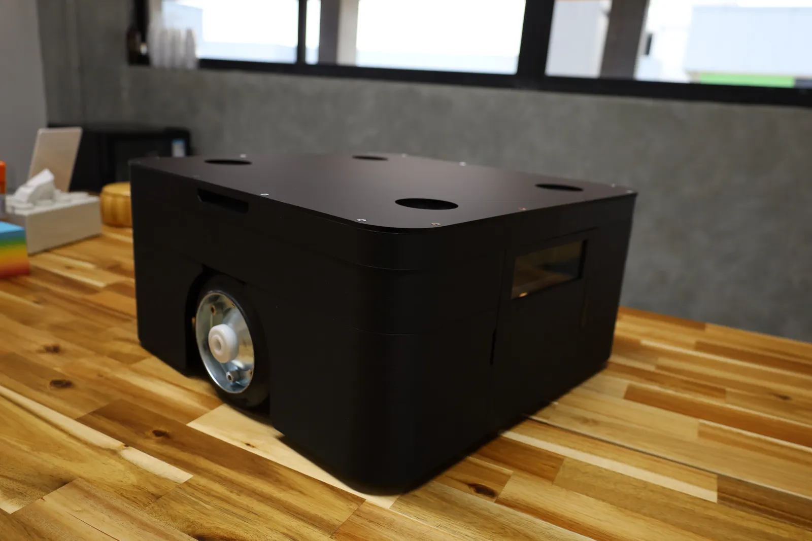 The finished matte black cover on Oriental Motor's AGV, seen from a front corner on a wooden table, with the drive wheel showing through its cut-out