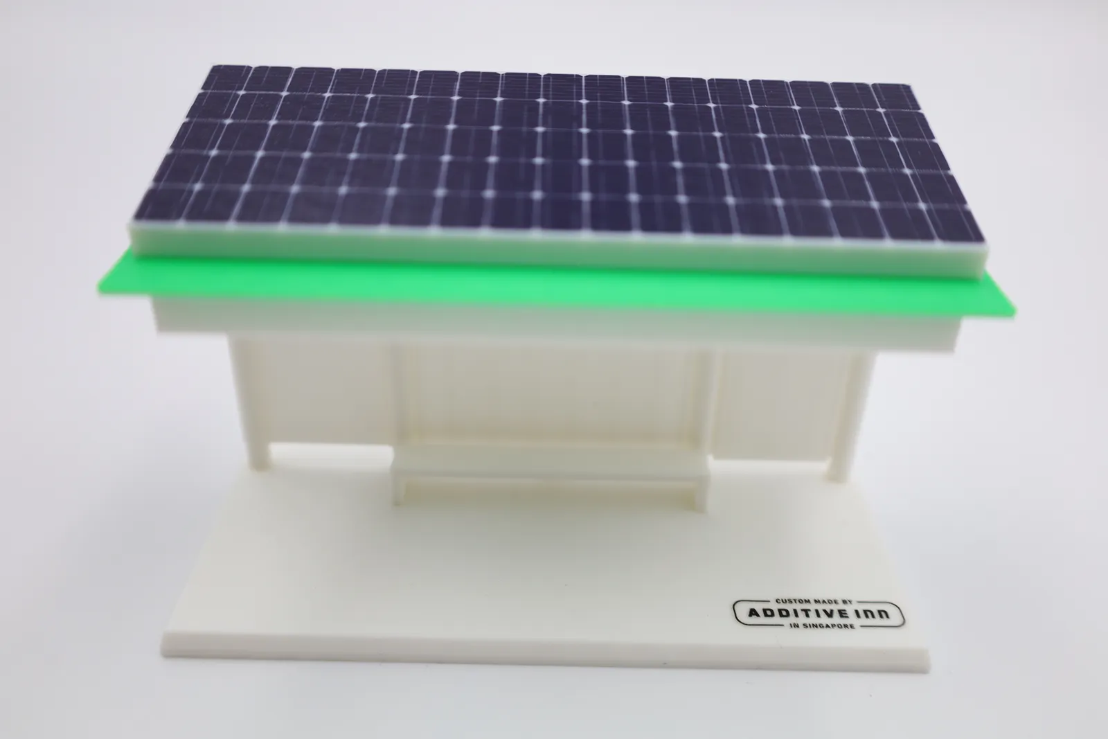 The finished bus stop model at an angle: a solar panel roof over a bright green roof plate, white panelled walls and a bench on a white base