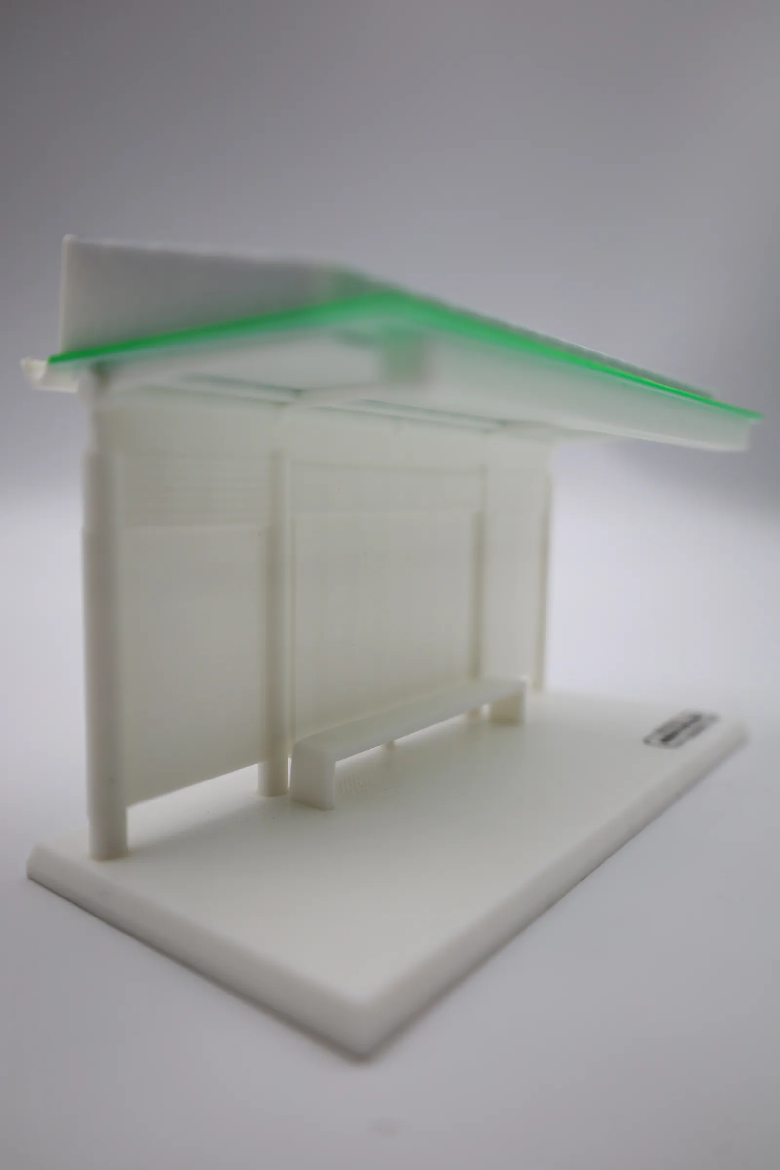 The finished model from a low angle at one end, showing the sloped roof above the white walls and the bench
