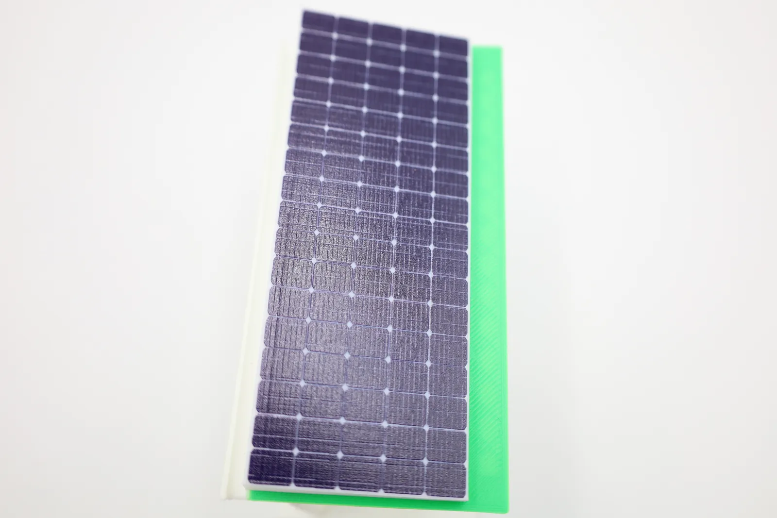 Looking down the length of the roof: rows of printed solar cells on the white block, with the green roof plate beside it