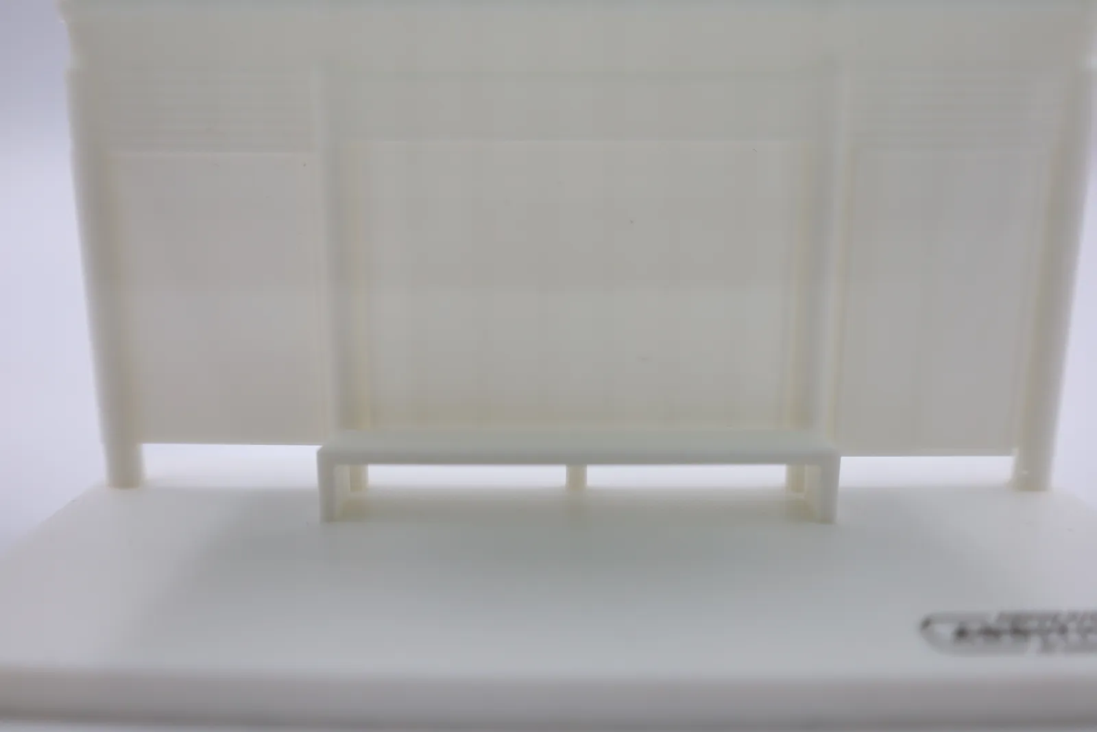 Close-up of the white bench on its legs in front of the panelled back wall, with louvres along the top