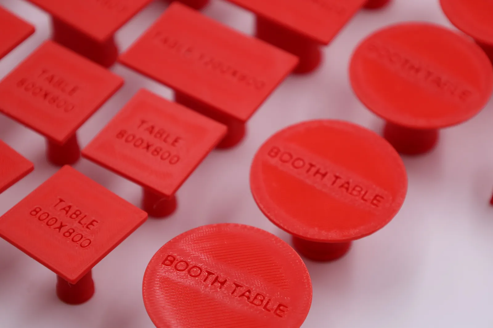 Close up of red tables with their names printed into the top: TABLE 800X800 on the square ones, BOOTH TABLE on the round ones