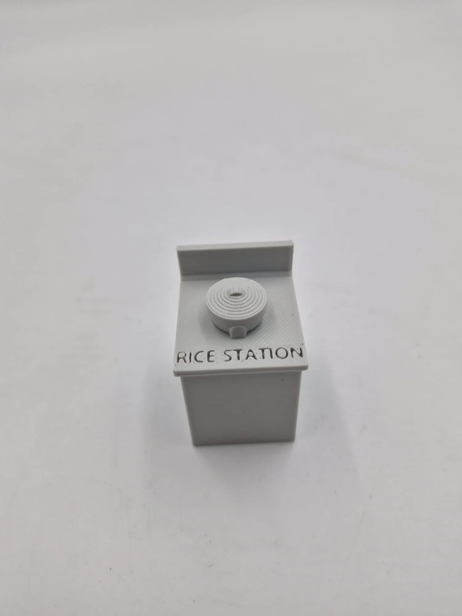 The modified rice station: a grey counter with a rice cooker on top and RICE STATION printed on the front
