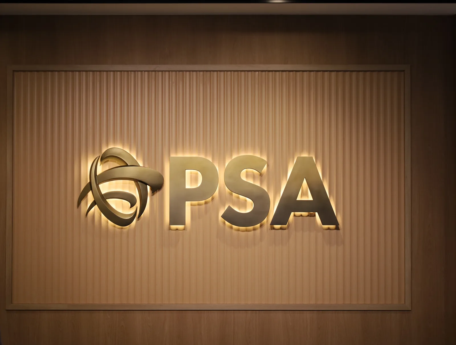 Close up of the halo-lit PSA logo: each brushed gold letter stands off the fluted panel, ringed by a soft glow