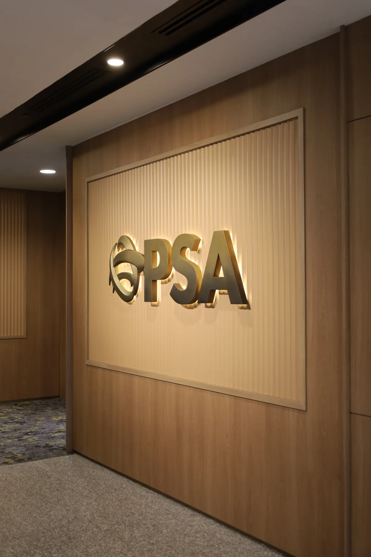 The PSA sign from the side, showing the depth of the brushed gold letters and the halo cast on the fluted panel behind