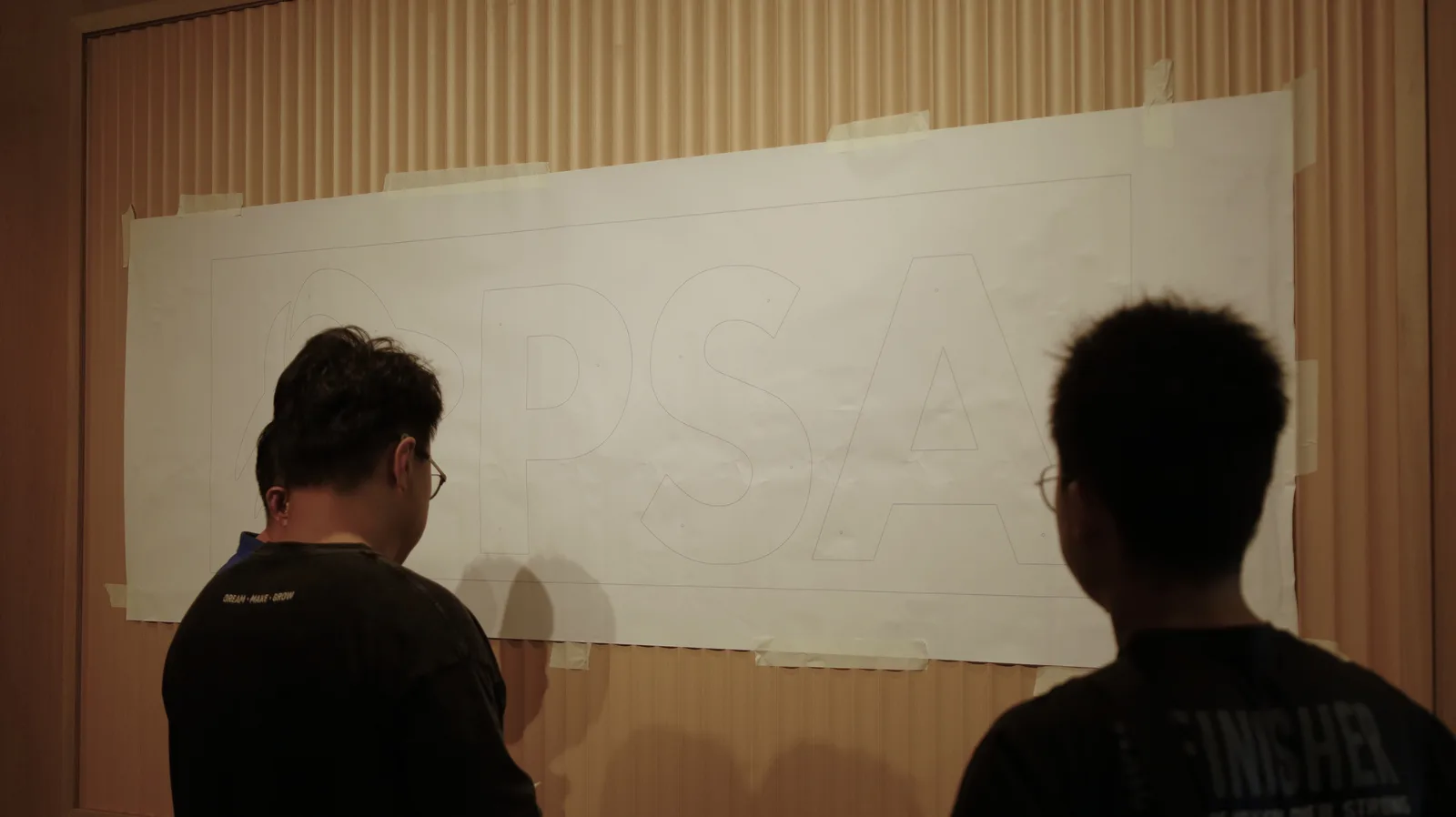Two of our team checking a full-size paper template of the PSA logo taped to the wall before installation