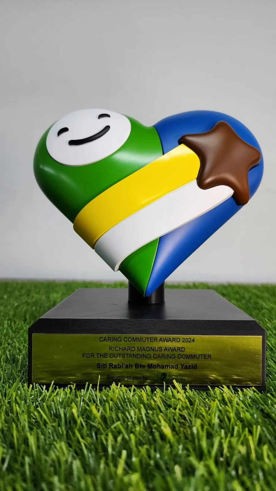 The 2024 Richard Magnus Award: a green and blue heart with a yellow and white band and a brown star, on a black base with a gold plate