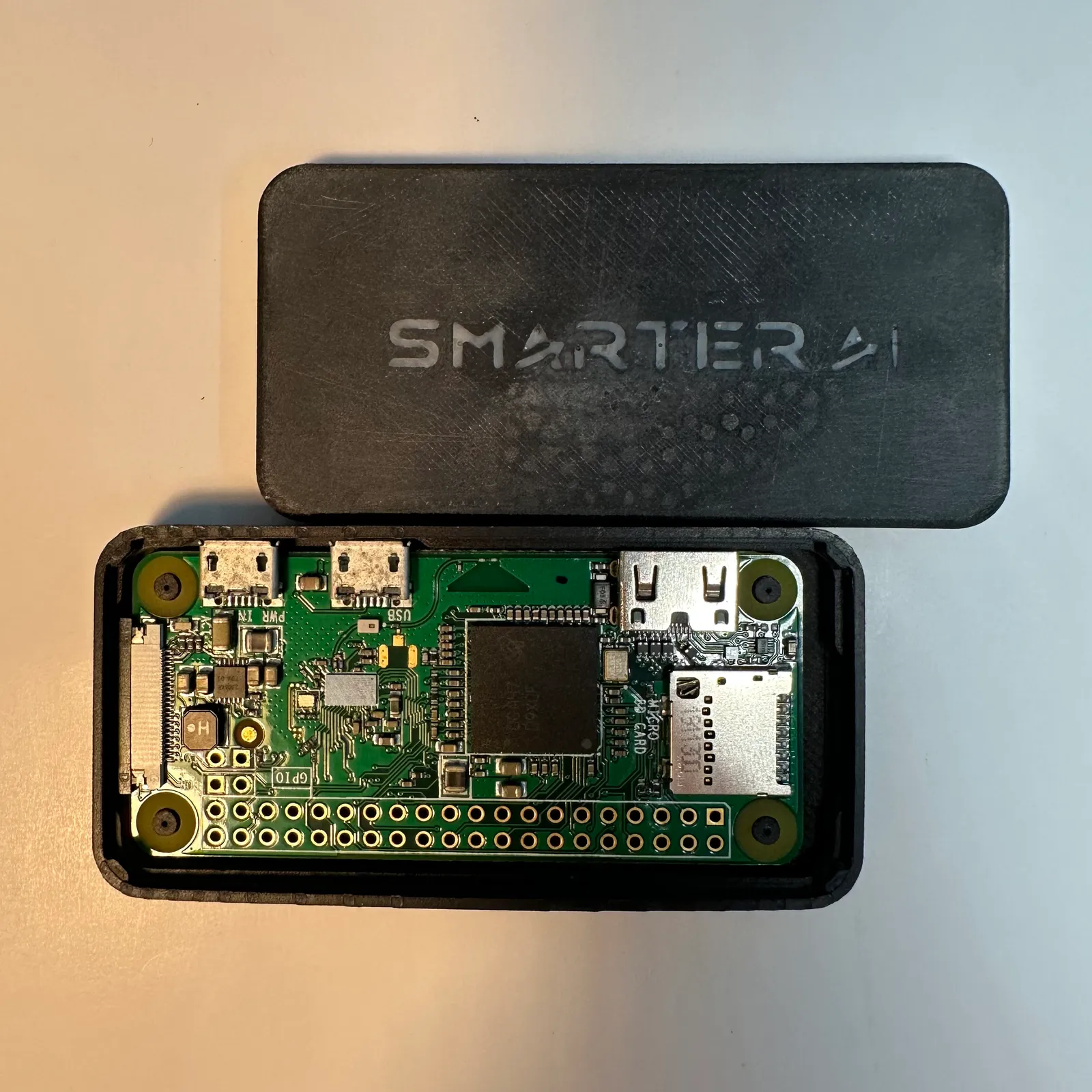 Top view of the finished case with the Raspberry Pi Zero inside and the black lid beside it, lettered SMARTER AI in grey
