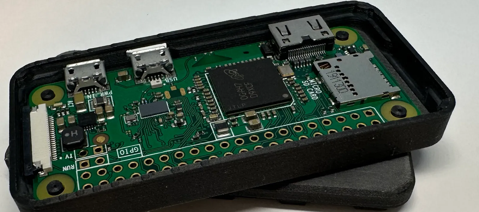 Close-up of the Raspberry Pi Zero in the open base, with a black post through each corner mounting hole and the walls close around the board