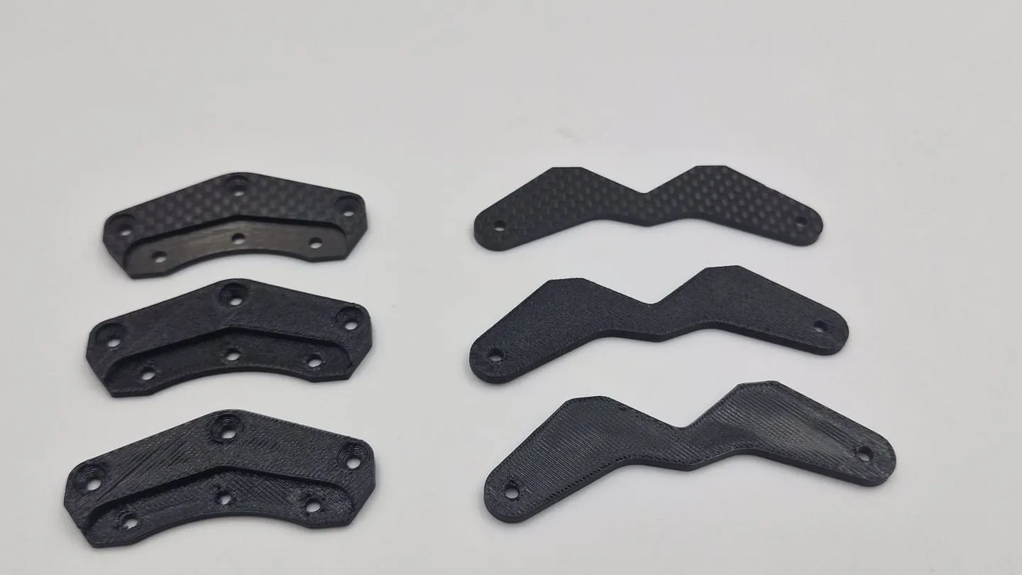Six black plates in two columns on a white table: the client's two carbon fibre originals on top, with two 3D printed copies of each below