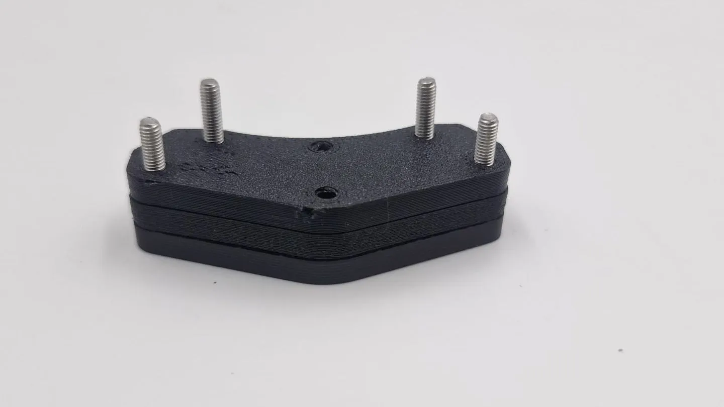 The four-stud bracket close up: three black plates stacked flat, with four steel studs standing up through the top plate