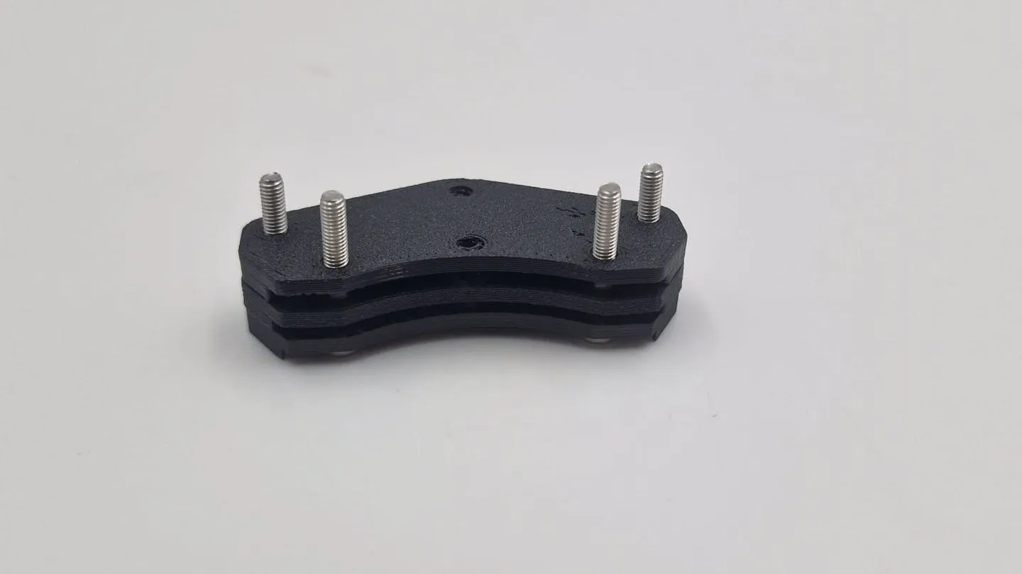 The finished four-stud bracket at an angle: three black plates stacked flat, with four steel studs standing up from the top