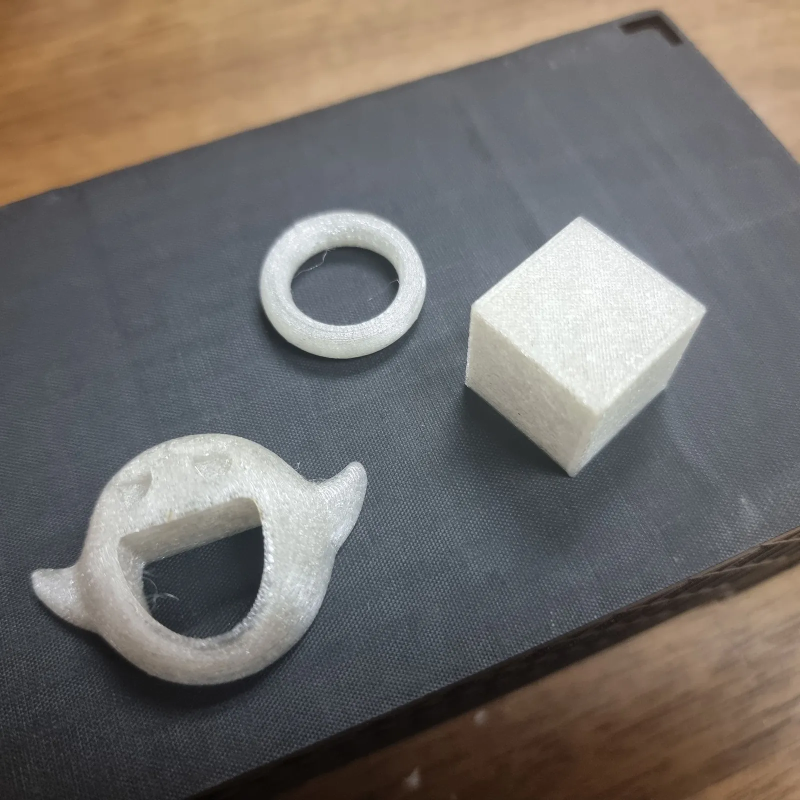 Close-up of three small white test prints with a speckled translucent look: a ring, a ghost with an open mouth and a cube