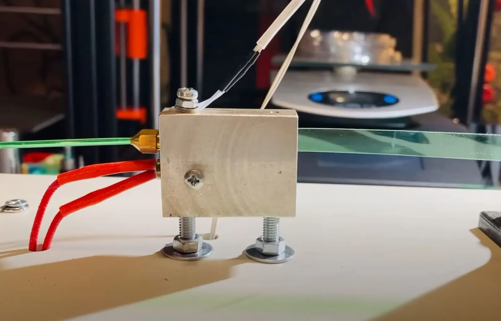 The first test rig: green bottle strip entering a metal heating block on bolts and leaving its brass nozzle as round filament