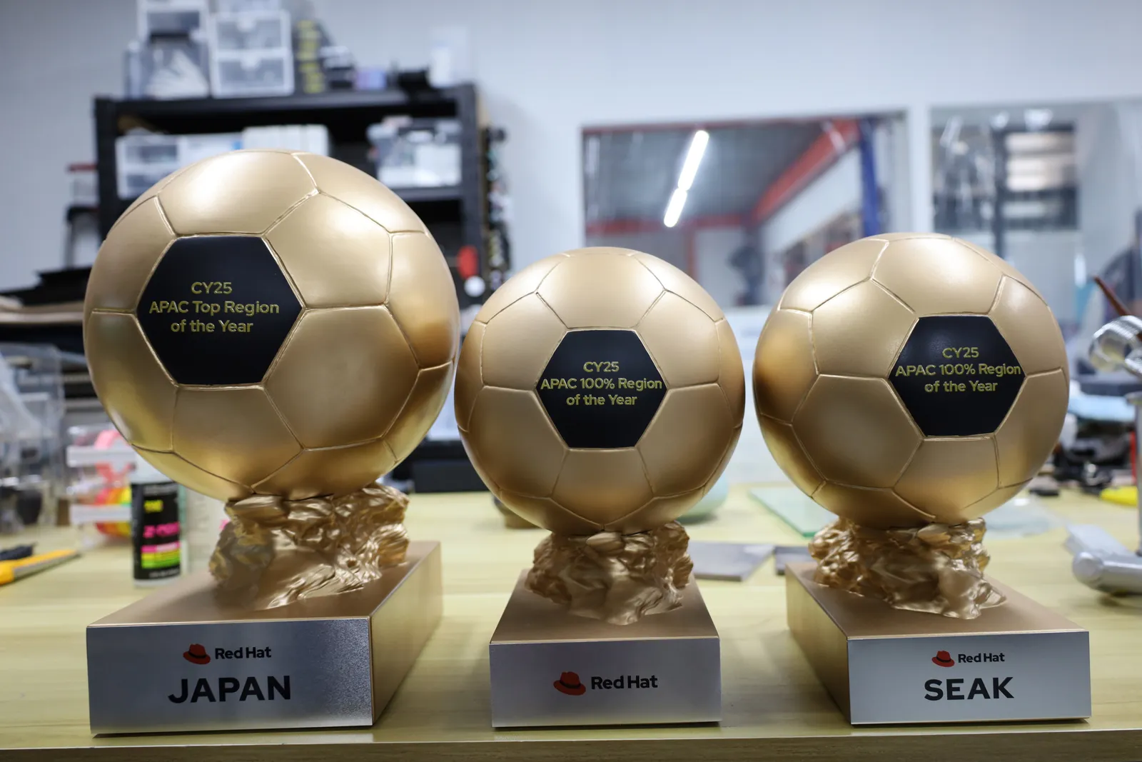 The three finished trophies in a row on our workbench: the large Top Region of the Year ball on a JAPAN plate, a 100% Region ball with the Red Hat logo and a 100% Region ball on a SEAK plate