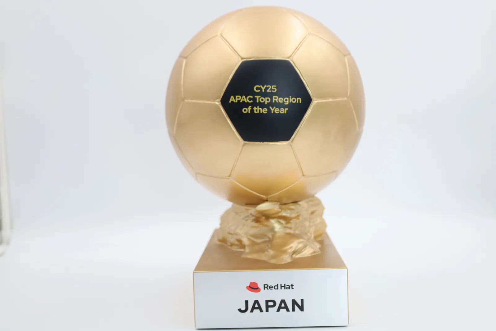 The Top Region of the Year trophy on its own against a white backdrop, the gold ball on a sculpted rock above a Red Hat JAPAN plate