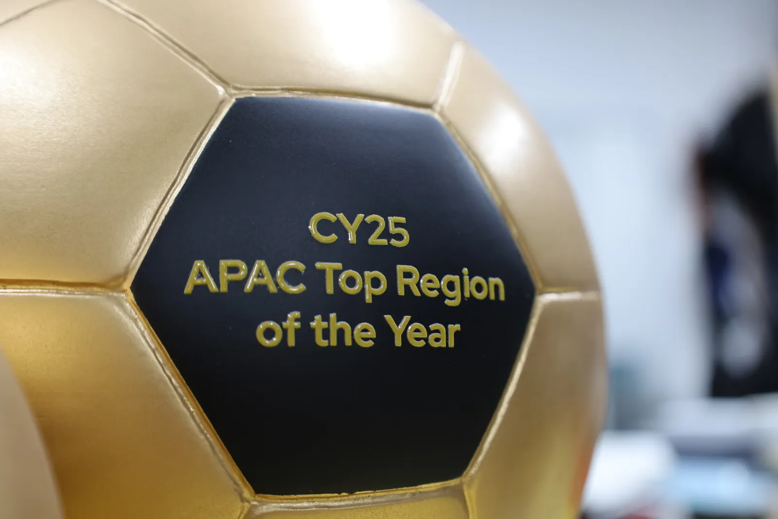 Close-up of the black hexagon panel on the gold football, lettered CY25 APAC Top Region of the Year in gold