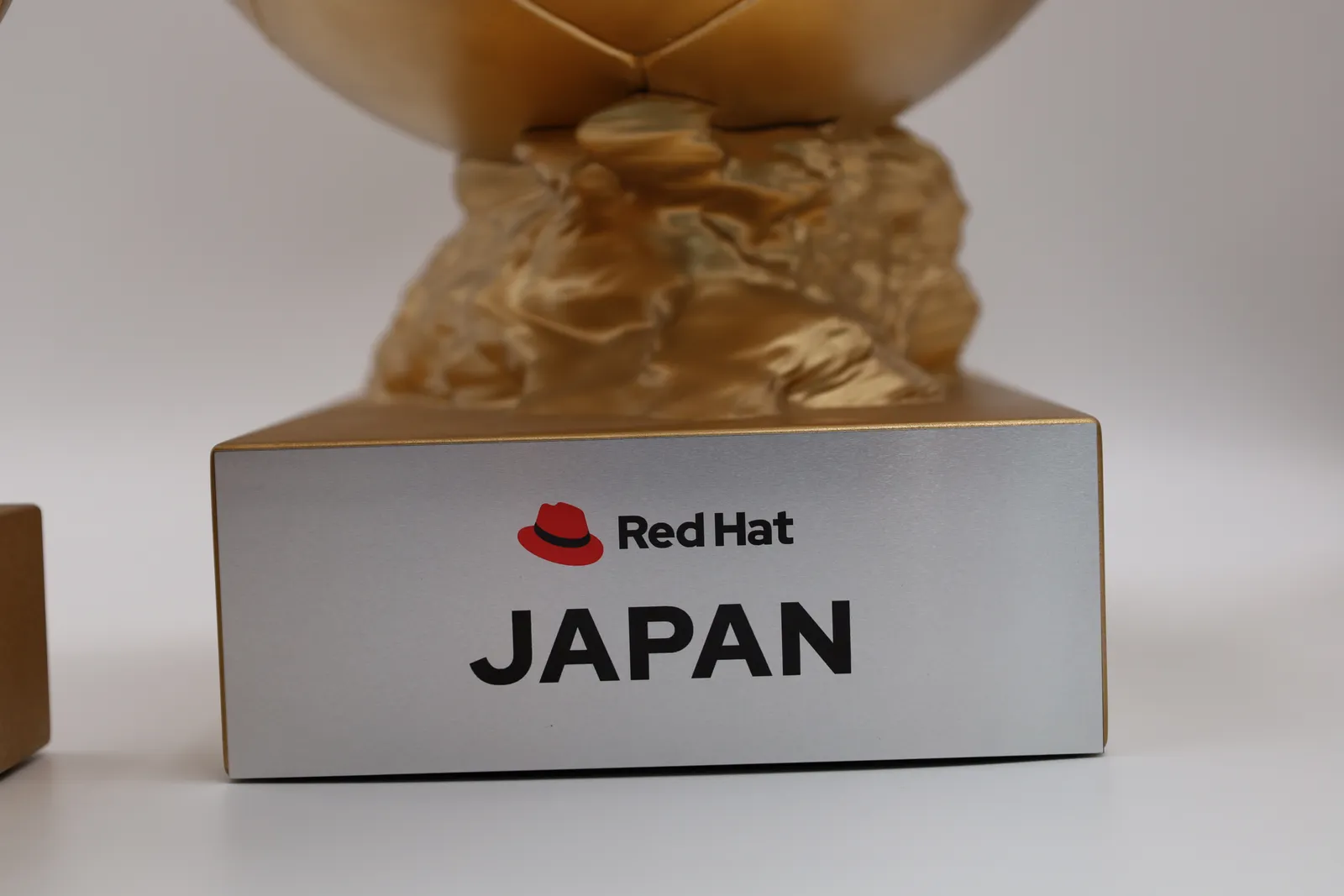 Close-up of a gold base with a brushed silver plate reading Red Hat above JAPAN, the sculpted gold rock on top