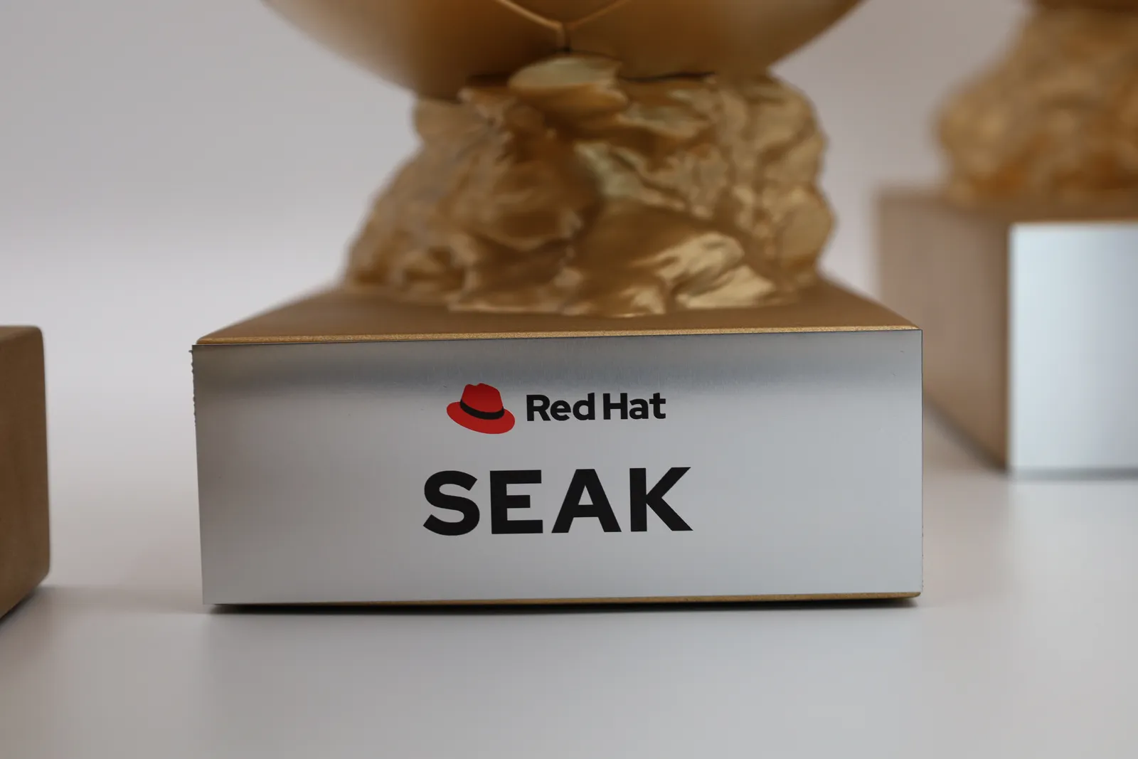 Close-up of a gold base with a brushed silver plate reading Red Hat above SEAK, the sculpted gold rock on top
