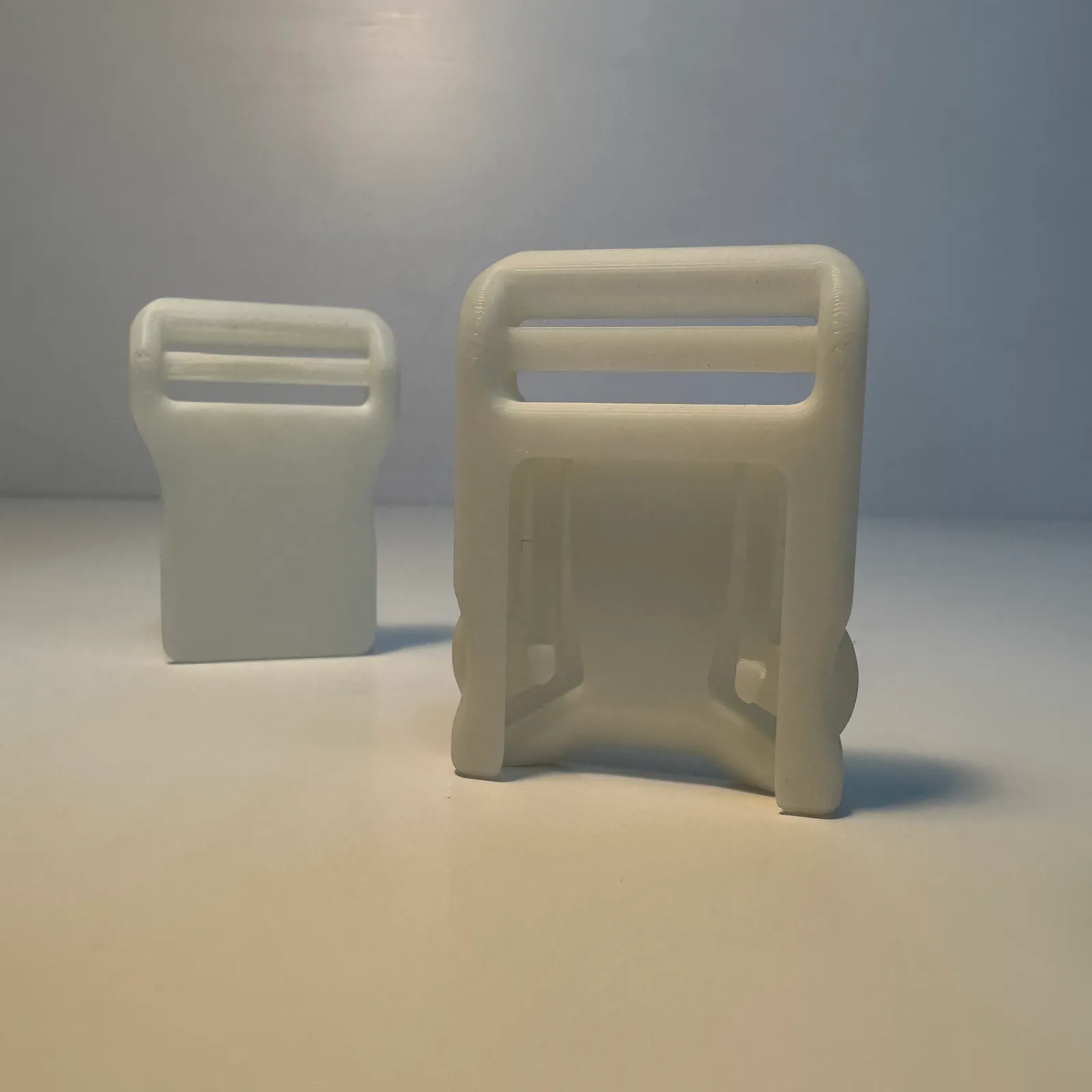 The two printed halves standing upright on a white table, apart: the flat socket on the left and the larger clip with its strap slot on the right