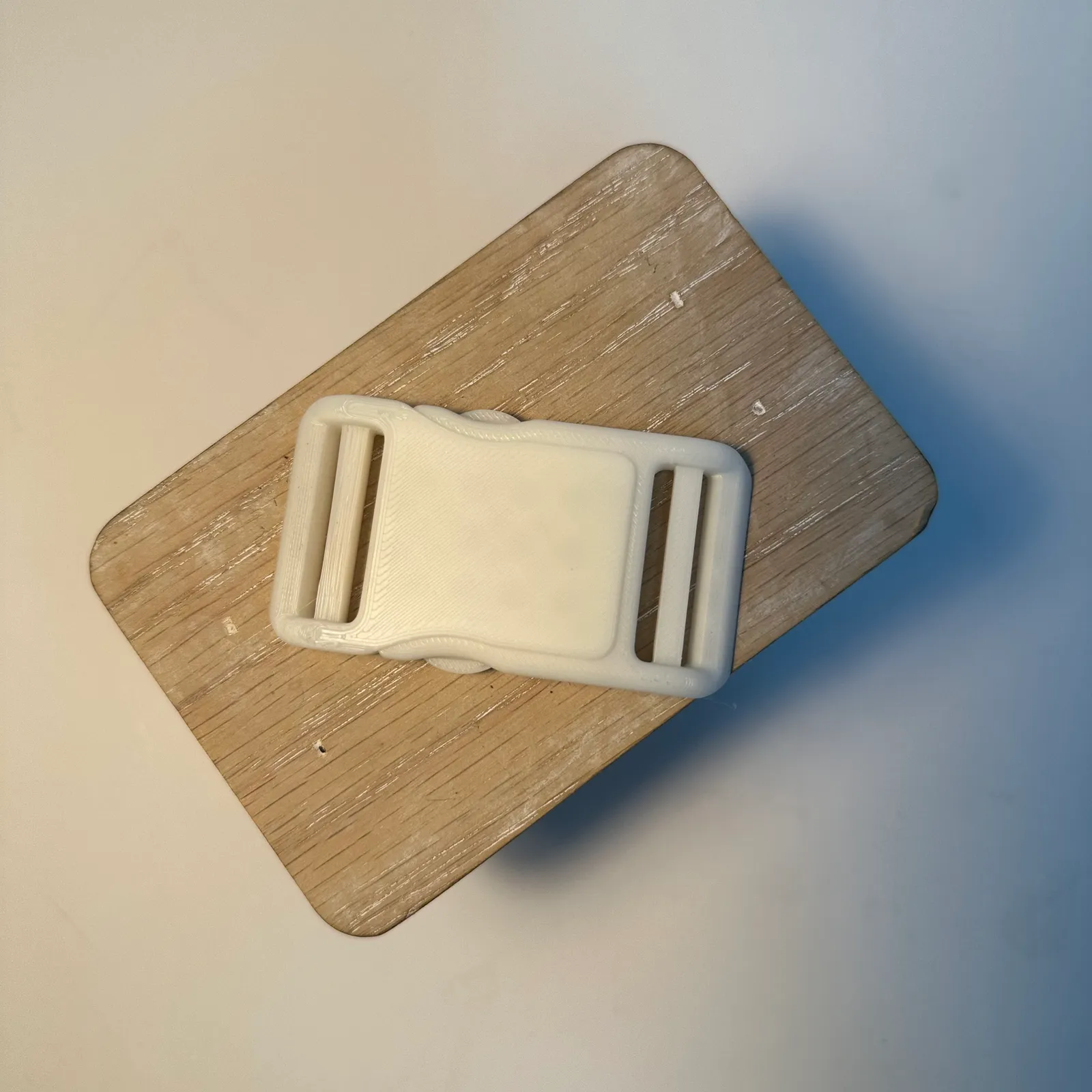 The finished buckle clipped shut on a wooden stand, seen from above, with a strap slot at each end