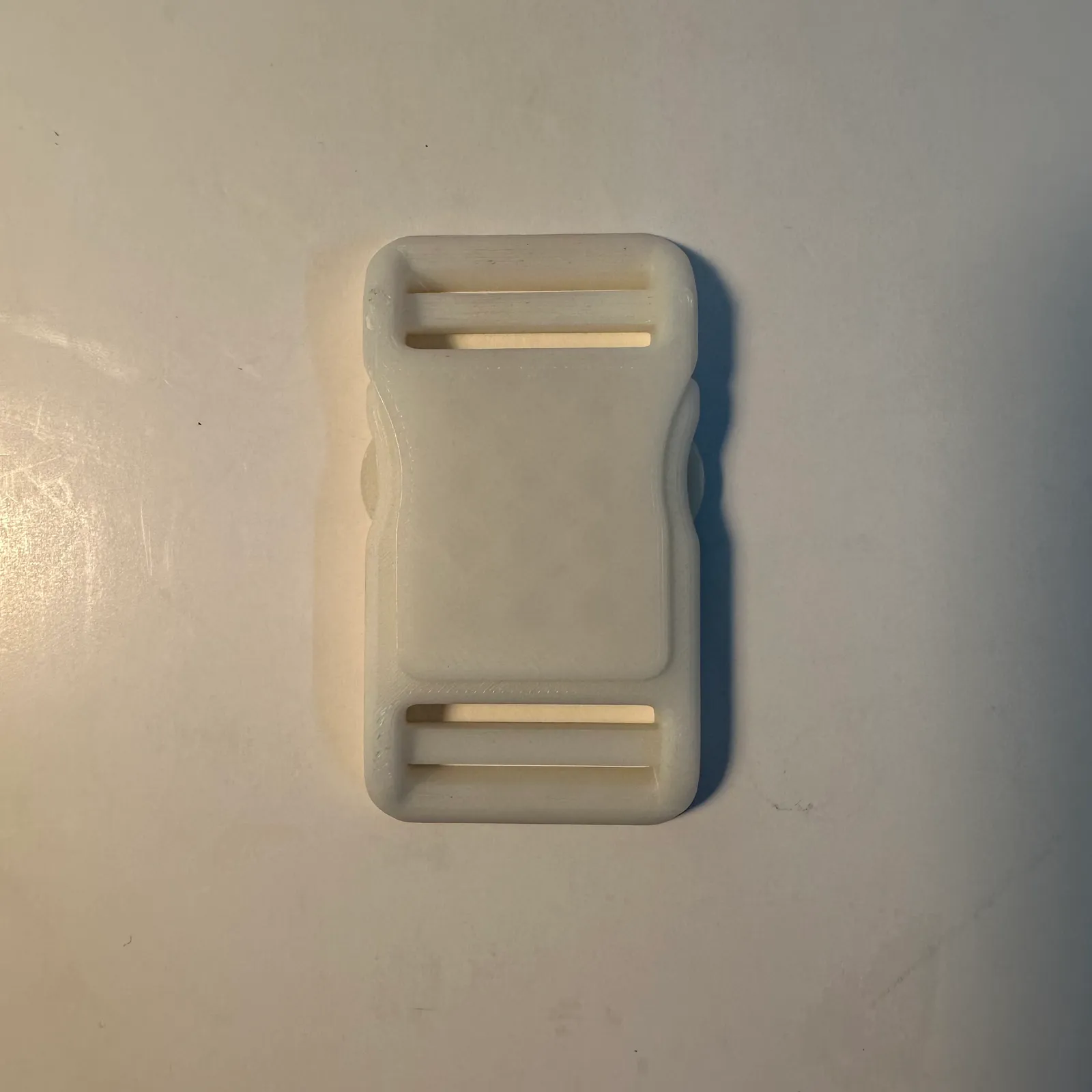 The clipped buckle lying flat on a white table, seen from above, with its strap slots at the top and bottom