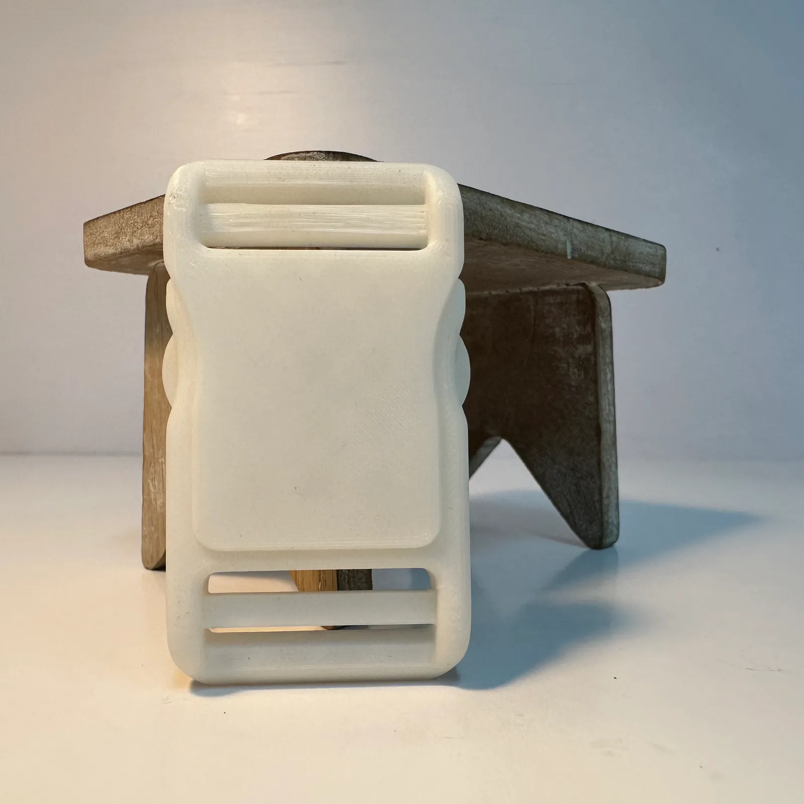 The clipped buckle leaning upright against a small wooden stool, showing its full length from one strap slot to the other