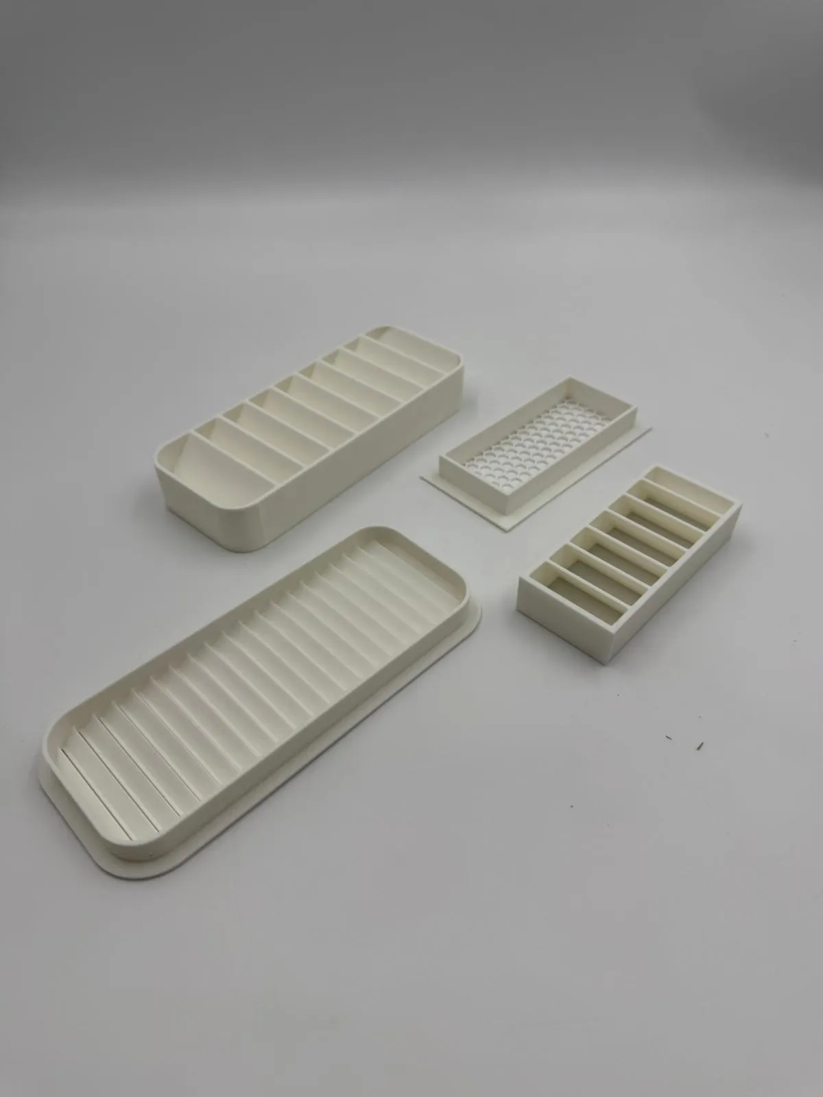 One set of four white 3D printed vent parts at an angle on a white background: an angled louvre, a large straight-slat vent, a small honeycomb vent and a horizontal louvre