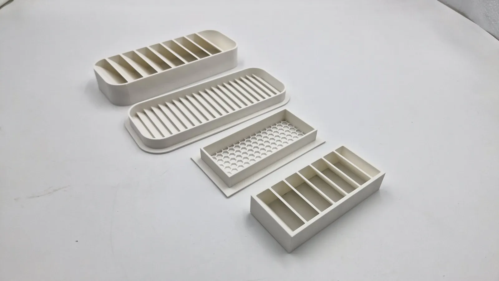 A finished set of four white PLA vent parts in a row on a white table, from the angled louvre at the back to the horizontal